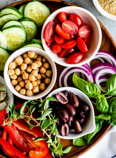 wooden circle tray full of white bowls with fresh ingredients for vegetarian Mediterranean recipes.