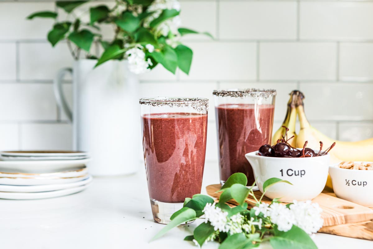 healthy smoothie in 2 glasses with cups of cherries and cashews next to them.