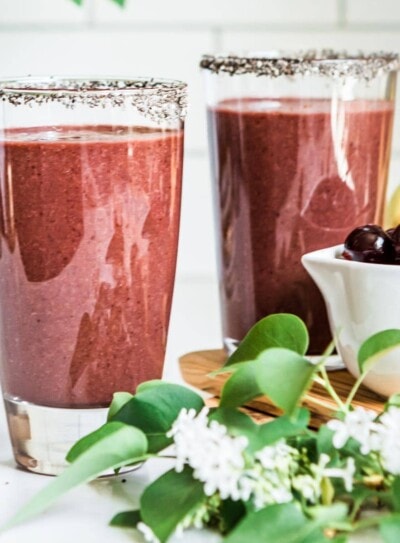 2 açai smoothies in glasses rimmed with chia seeds, next to bowls of cherries and cashews.