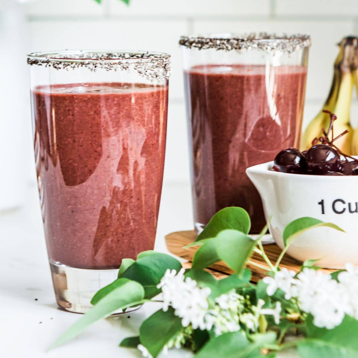 2 açai smoothies in glasses rimmed with chia seeds, next to bowls of cherries and cashews.