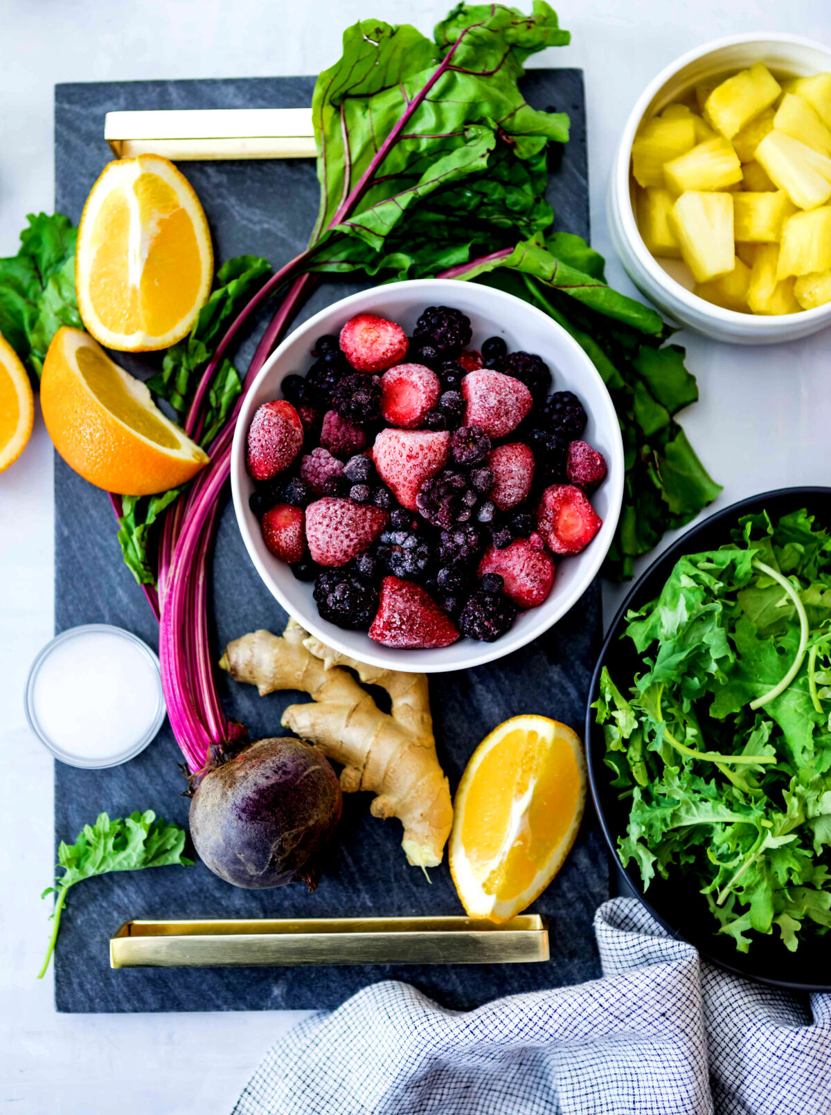 A bowl full of berries, on a countertop, surrounded by fresh ingredients: lemon, beetroot, ginger, greens, and more, ready to make the best anti-inflammatory smoothie recipe.