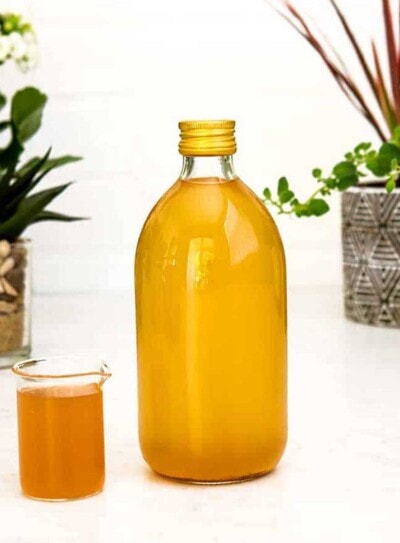 apple cider vinegar drink in a small glass next to a large glass jar of homemade ACV.