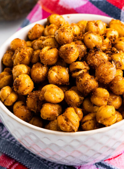 white bowl full of garlic baked chickpeas on top of a colorful tea towel.