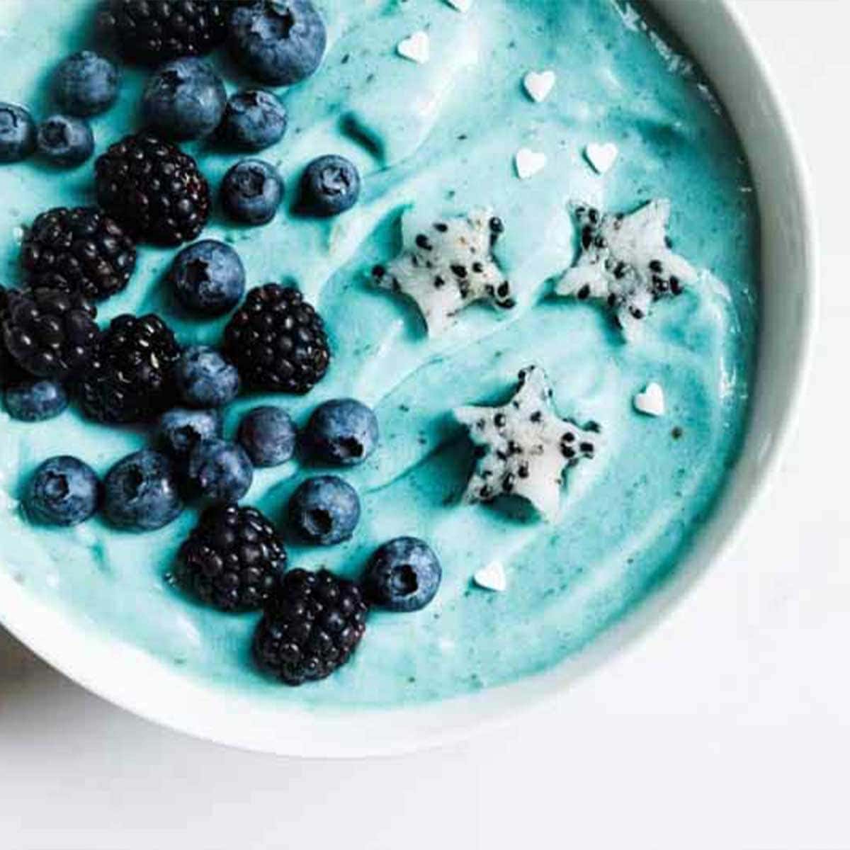 banana nice cream turned blue with spirulina powder in a white bowl topped with fresh fruit and white sprinkles.