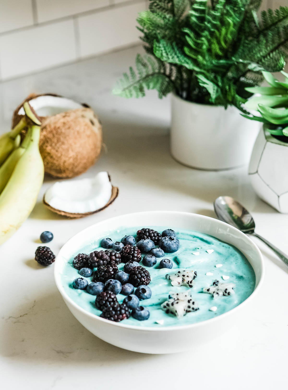 blue ice cream in a white bowl with fresh berries and dragon fruit stars.