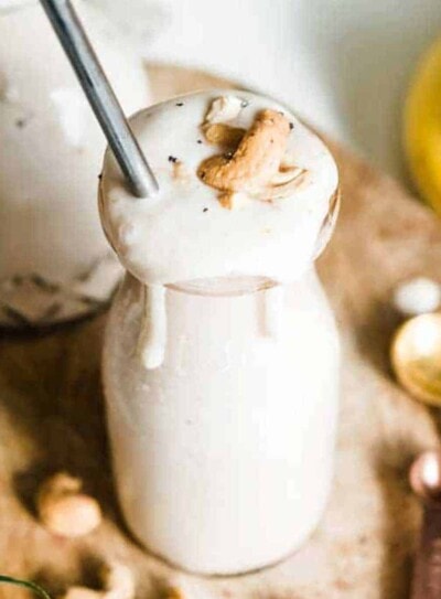 banana smoothie in milkshake glass topped with cashews and metal straw.