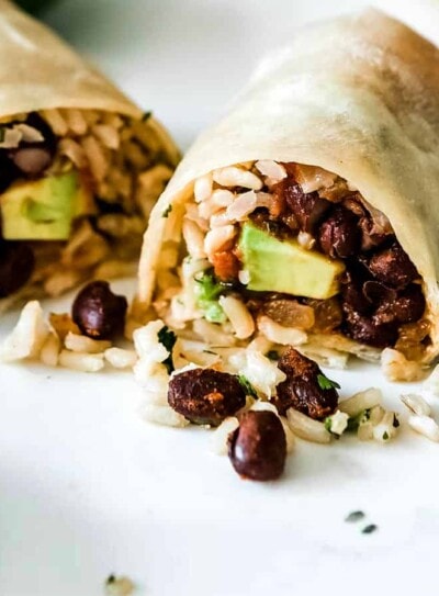 2 bean and rice burritos cut open and showing the ingredients inside on a white counter top.