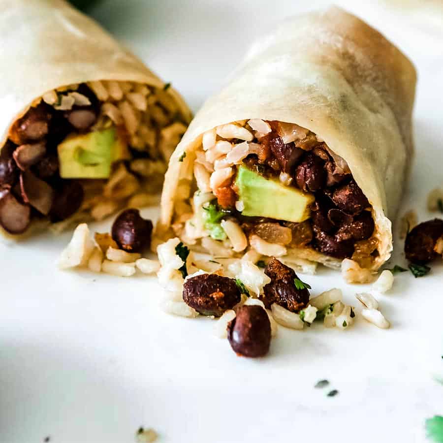 2 bean and rice burritos cut open and showing the ingredients inside on a white counter top.