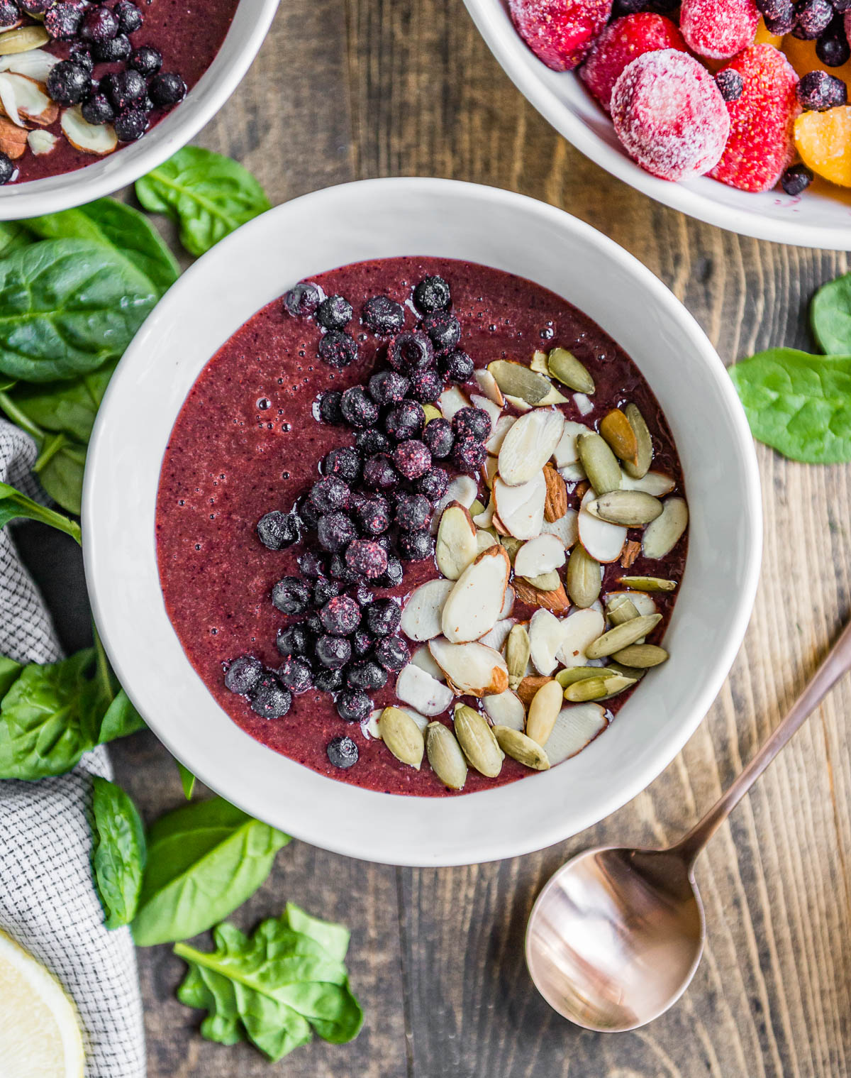 berry smoothie bowl in white bowl topped with frozen berries, sliced almonds and pepitas.