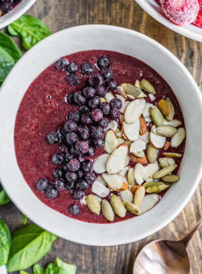 berry smoothie bowl in white bowl topped with frozen berries, sliced almonds and pepitas.