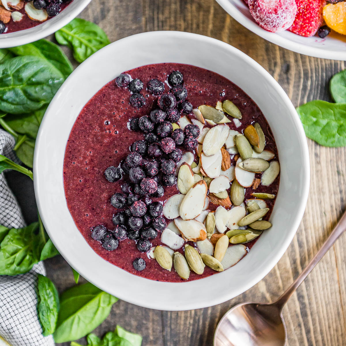 berry smoothie bowl in white bowl topped with frozen berries, sliced almonds and pepitas.