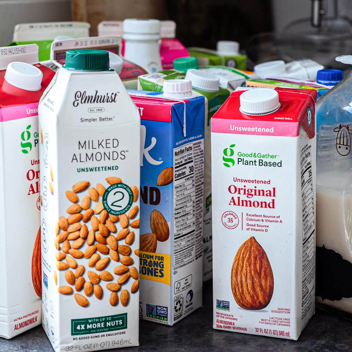 several cartons of different brands of store bought almond milk on a counter top.