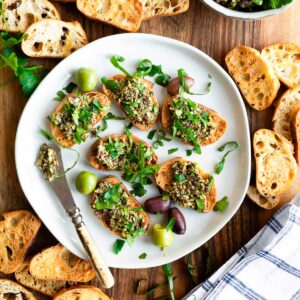 gray bowl full of green olive tapenade a topped with fresh parsley leaves.