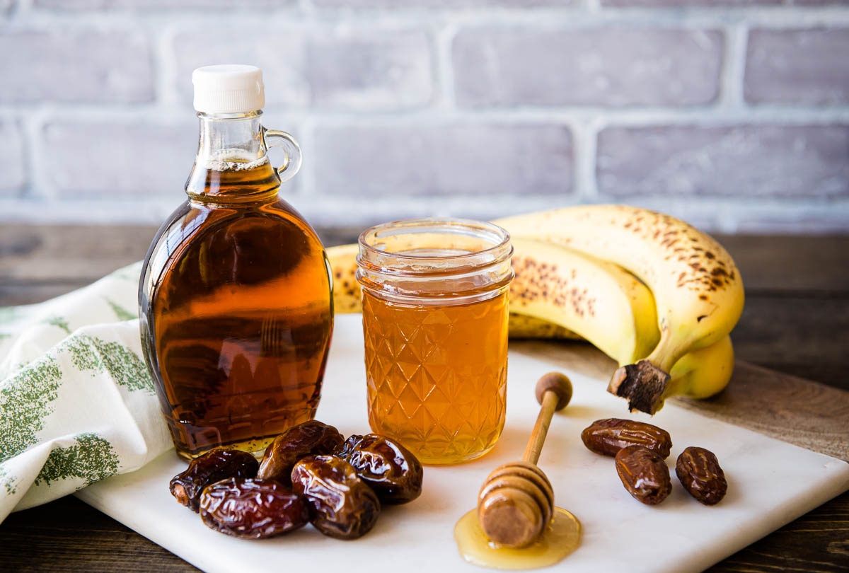 white marble cutting board topped with bananas, dates, honey and maple syrup.