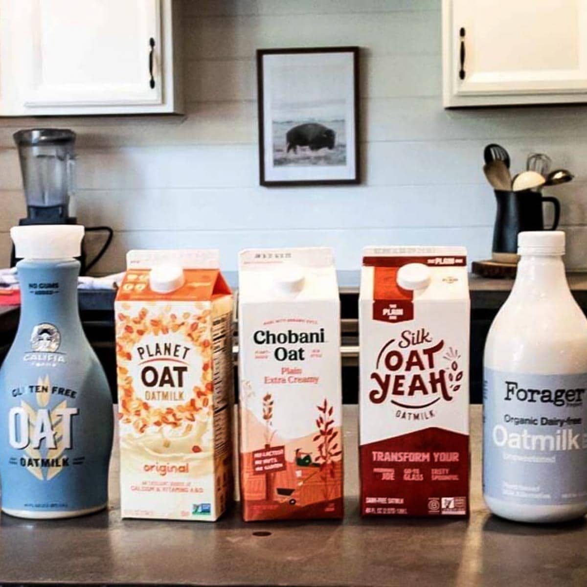 5 oat milk containers lined up on a kitchen counter, ready to be tested for the best oat milk brand.