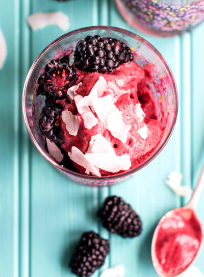 Blackberry coconut sorbet in clear glass on teal countertop with fresh fruit.