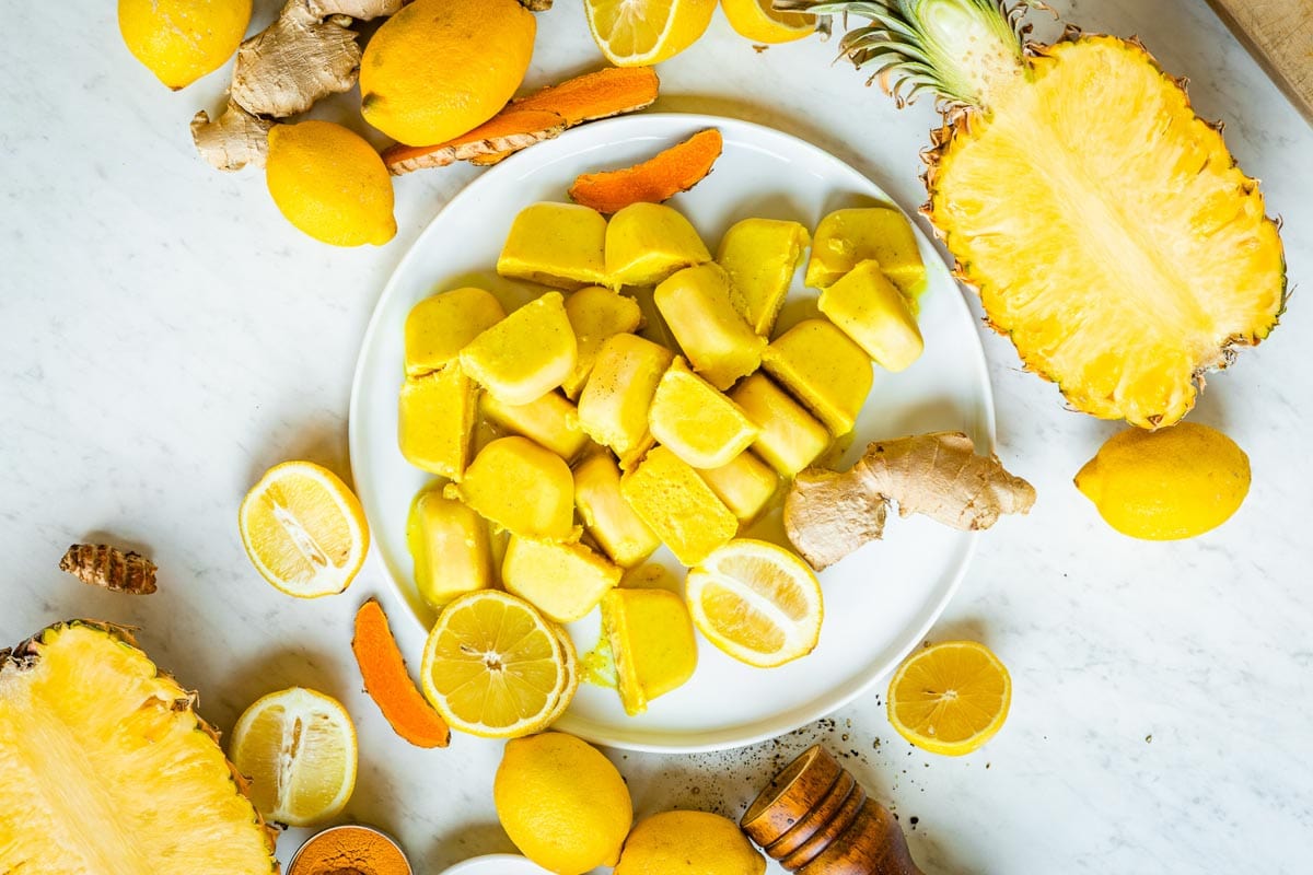 vibrant yellow smoothie cubes with fresh yellow and orange ingredients surround them like pineapple, lemon and turmeric.