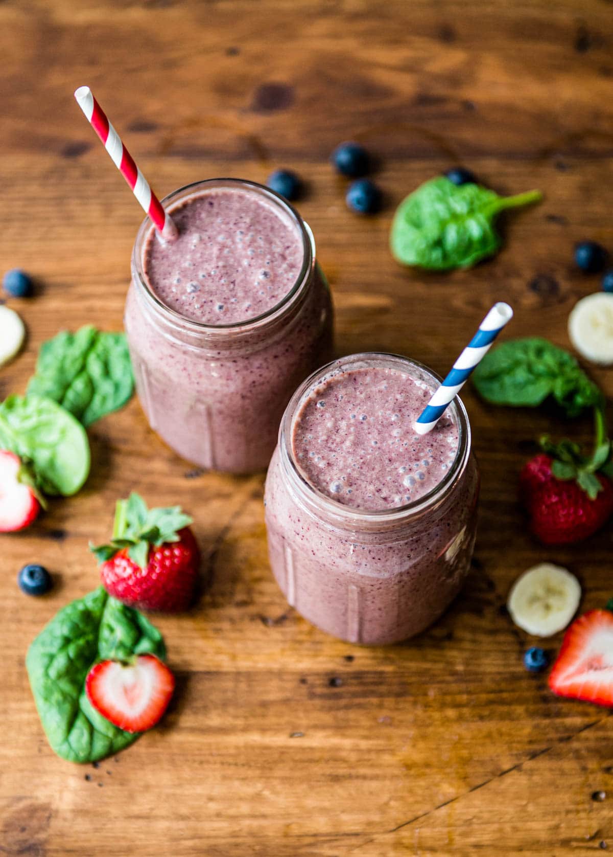 2 glasses of blueberry smoothie with paper straws.