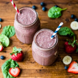 2 glasses of blueberry spinach smoothie with paper straws.