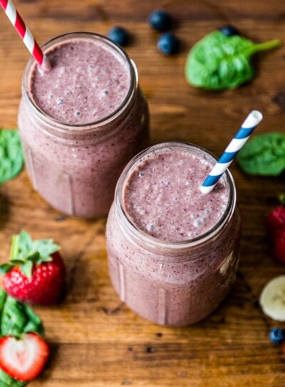 2 glasses of blueberry spinach smoothie with paper straws.