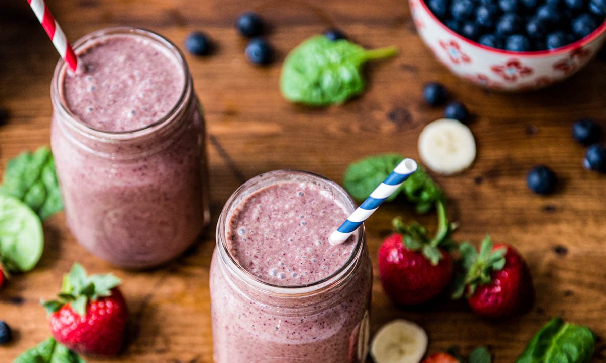 2 glasses of blueberry spinach smoothie with paper straws.