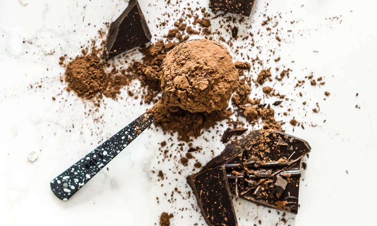 tablespoon scoop of cacao powder next to pieces of broken chocolate.