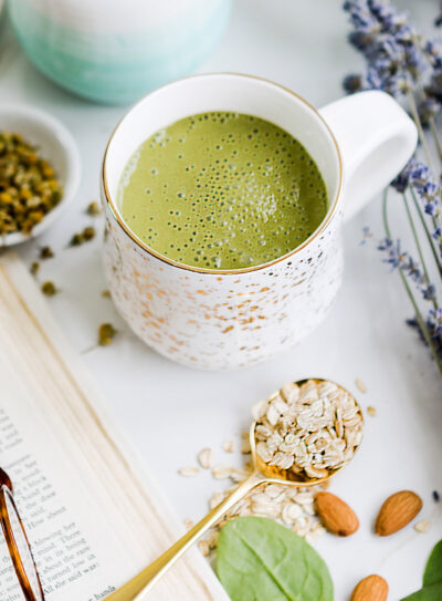 Green bedtime smoothie in two white mugs surrounded by lavender, almonds, tea, and spinach. A perfect healthy smoothie before bed to promote better sleep.