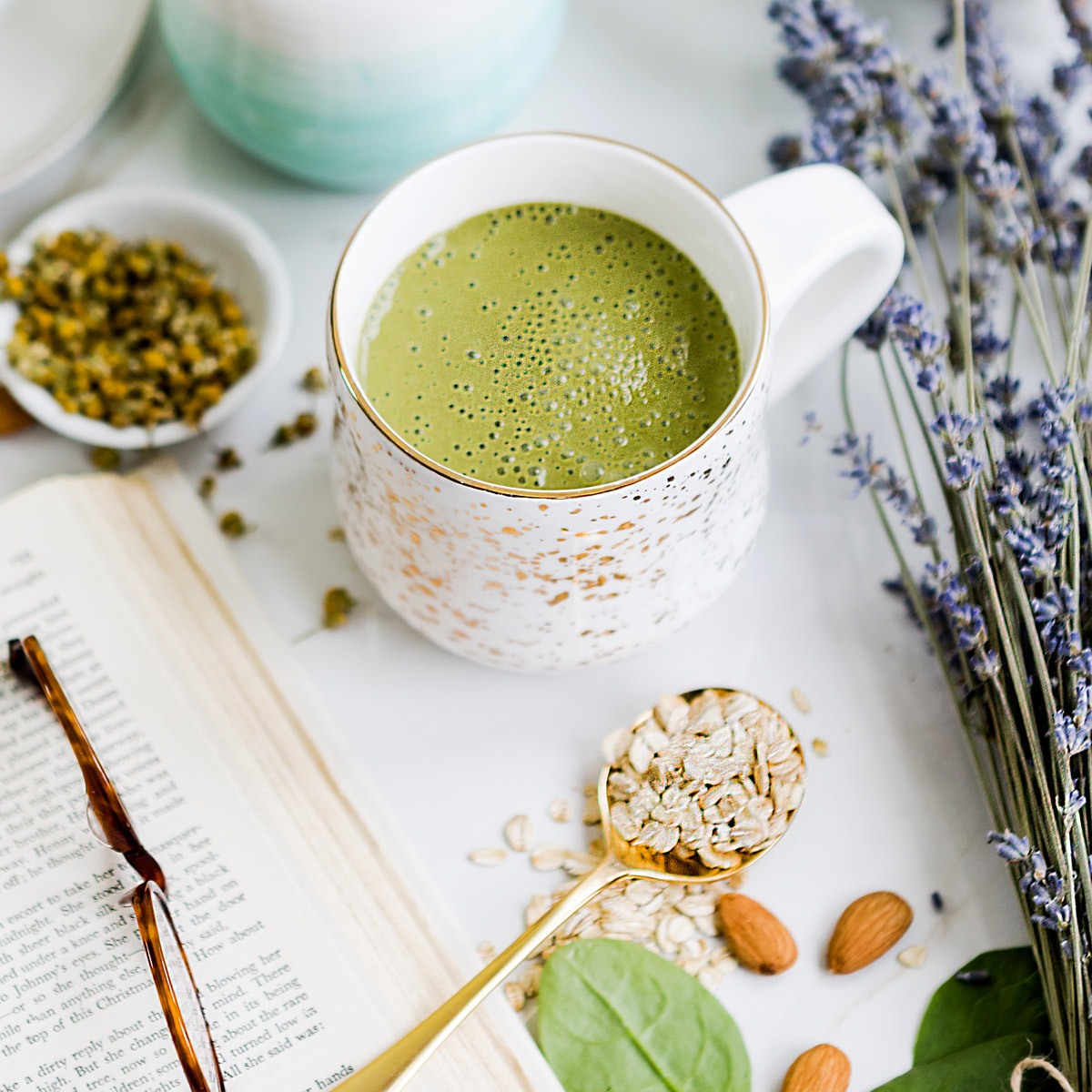 Green bedtime smoothie in two white mugs surrounded by lavender, almonds, tea, and spinach. A perfect healthy smoothie before bed to promote better sleep.