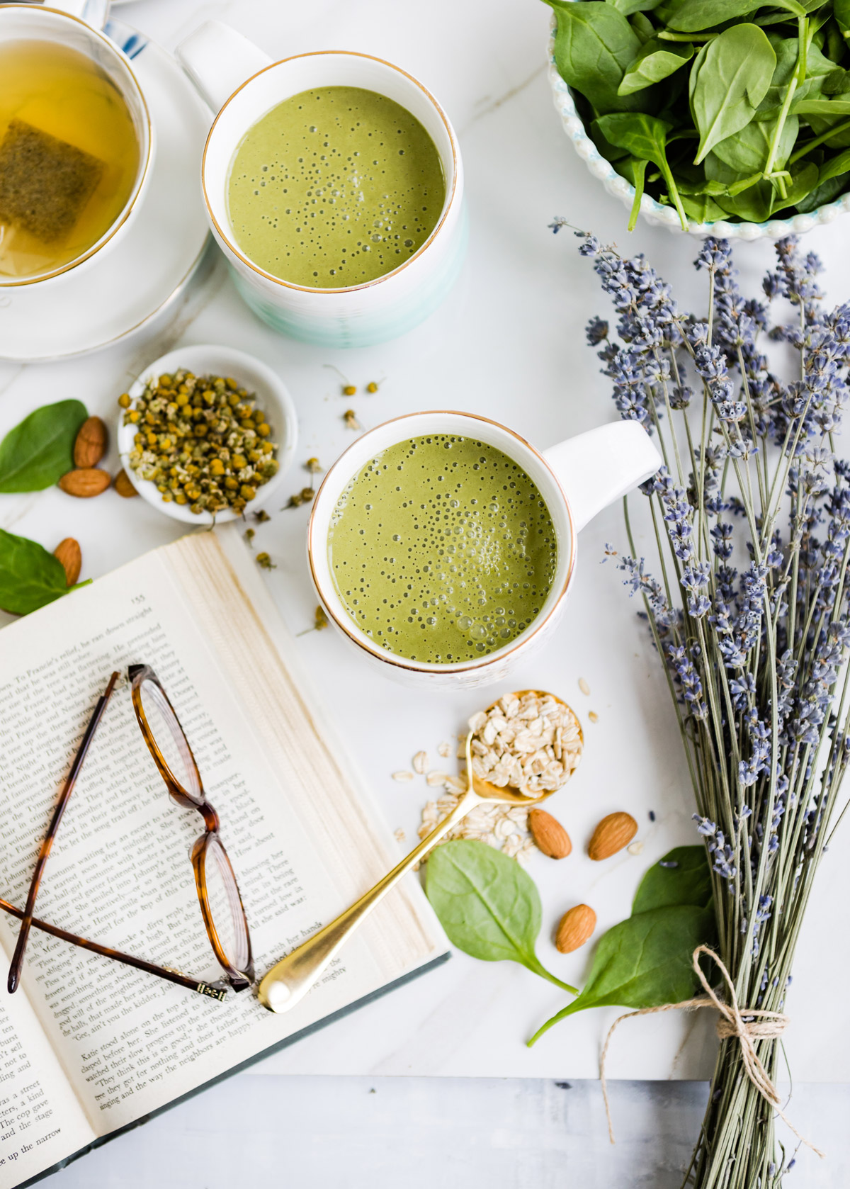 White mug with gold speckles filled with a green bedtime smoothie for sleep, surrounded by ingredients like oats and almonds.