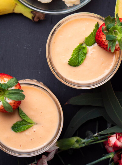 2 glasses with cantaloupe smoothies topped with mint leaves and fresh strawberries.