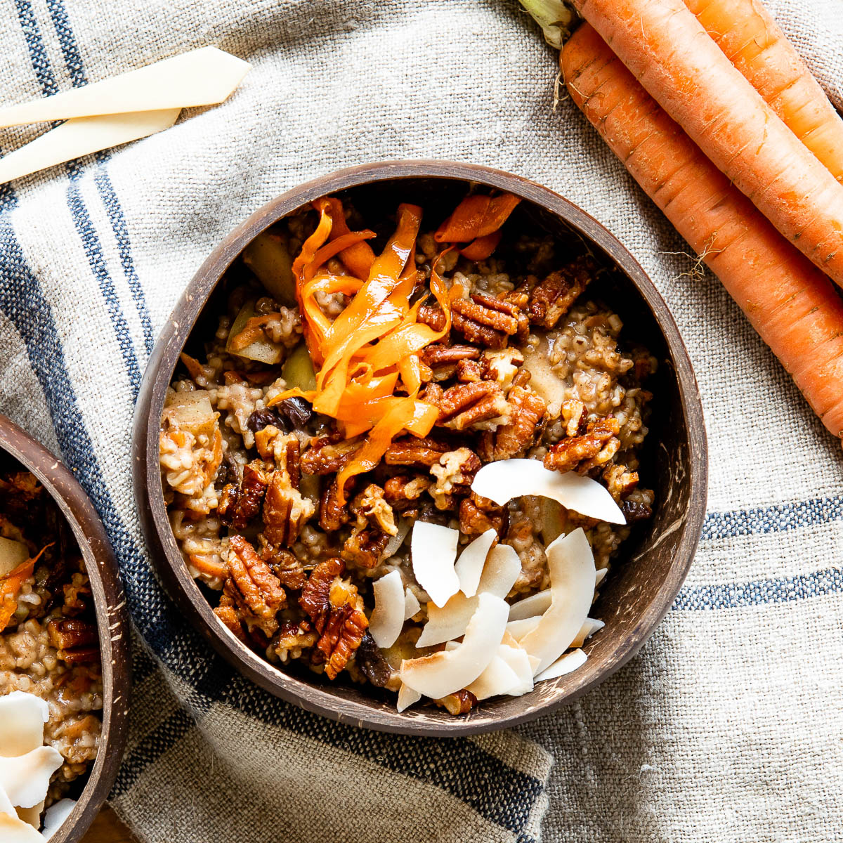 coconut bowl full of carrot cake oatmeal topped with candied pecans, coconut flakes and shredded carrots.