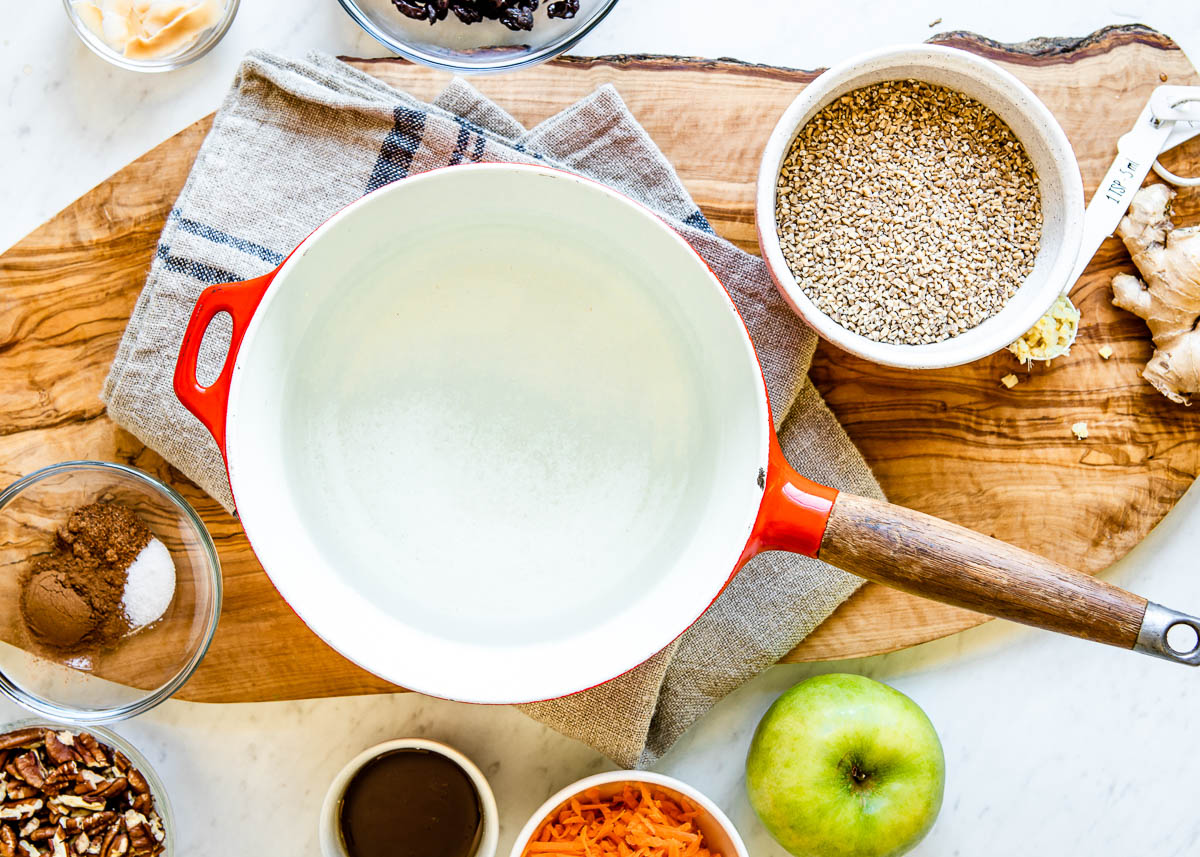 red bowl with wooden handle surrounded by small bowls of ingredients for carrot cake oatmeal.