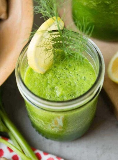 green celery smoothie in a glass jar topped with a lemon slice and fennel fronds.