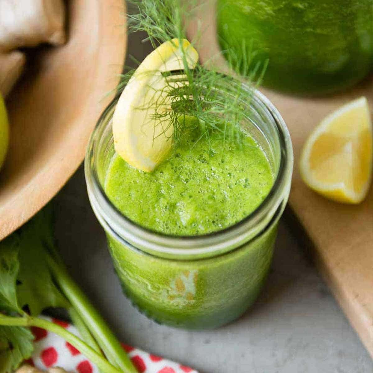 green celery smoothie in a glass jar topped with a lemon slice and fennel fronds.