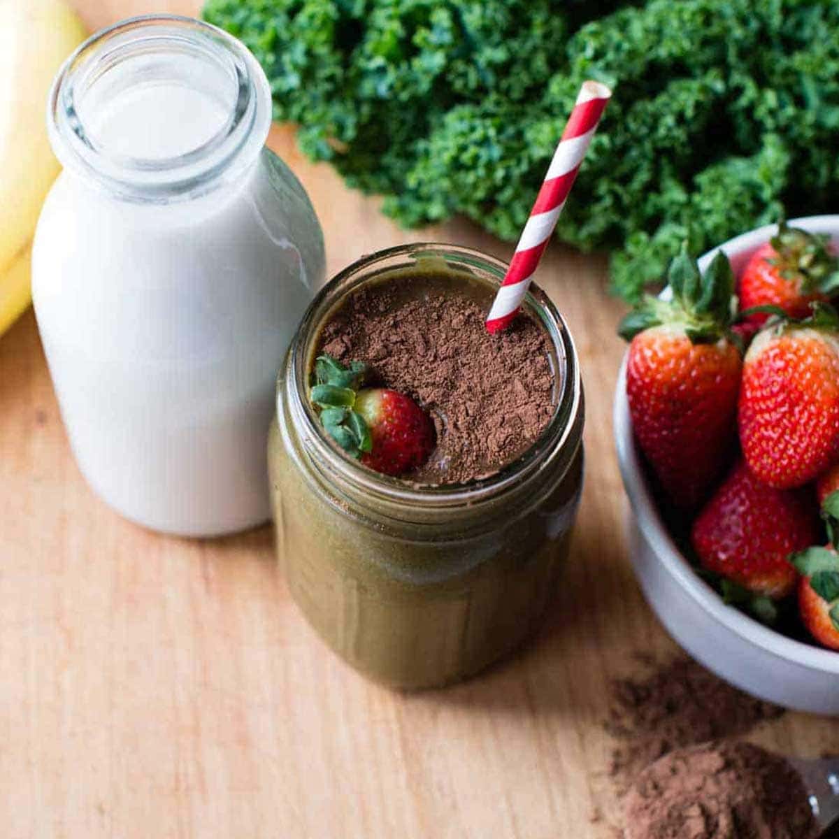 chocolate strawberry smoothie topped with cacao and fresh strawberries with a striped straw.