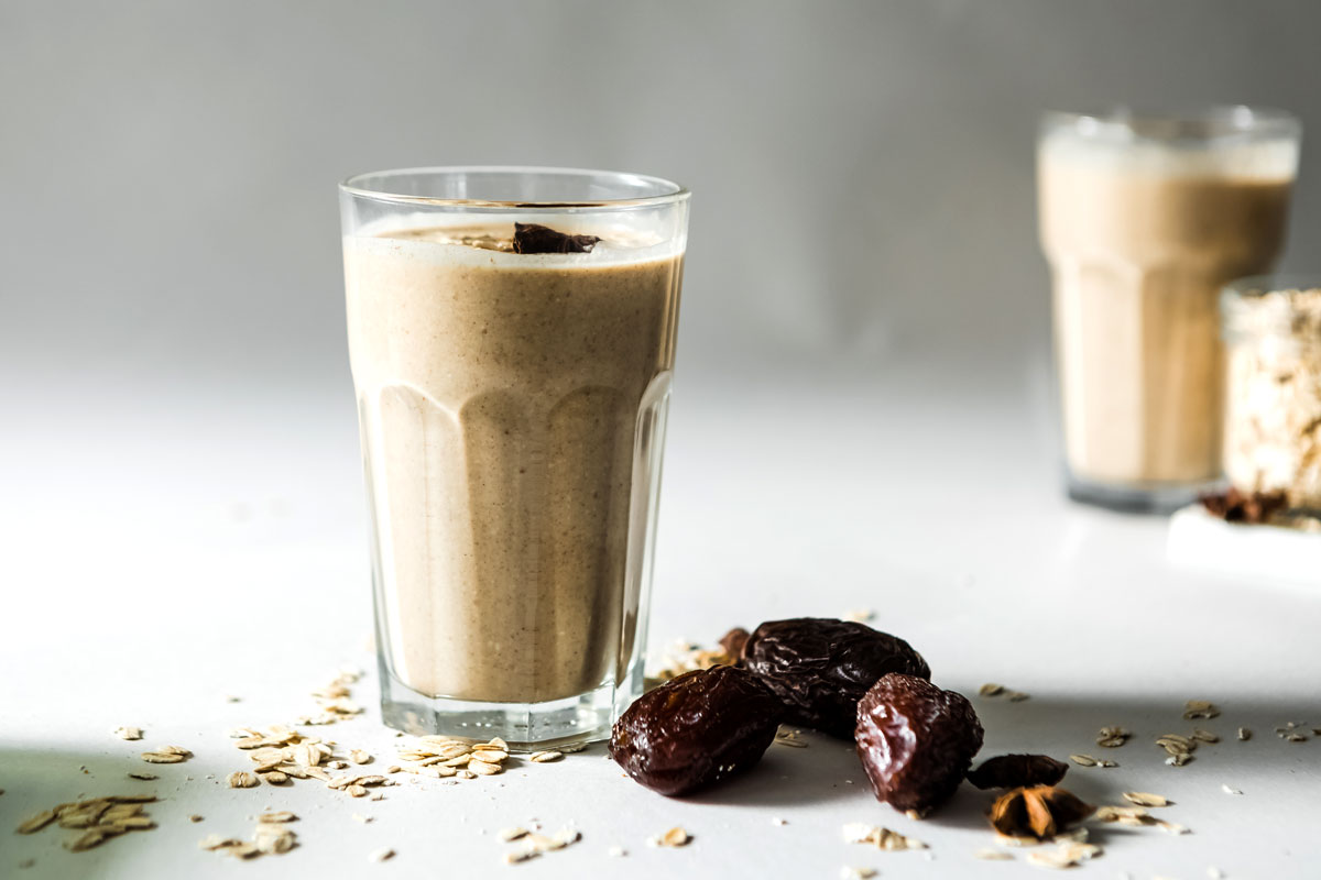 Healthy date smoothie topped with star anise and oats, served in a glass, featuring cinnamon and blended dates.