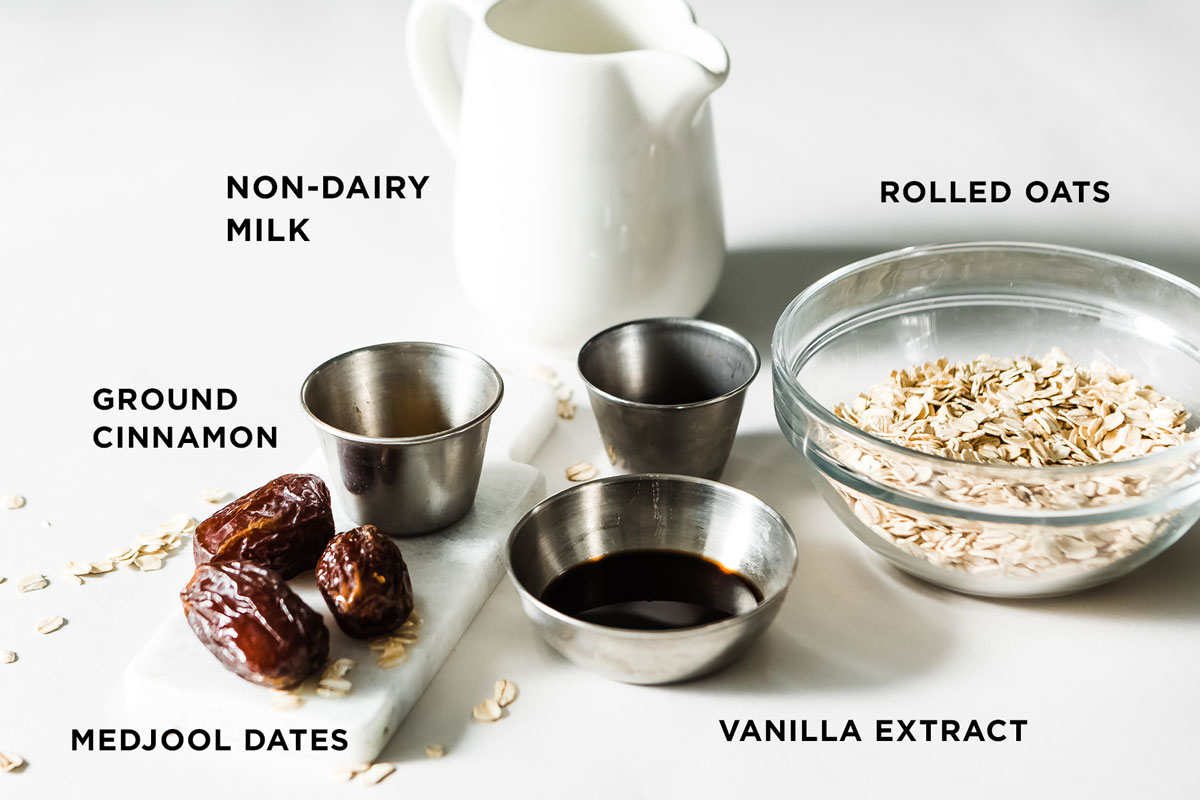 Ingredients for Date Smoothie Recipe including Medjool dates, rolled oats, vanilla extract, and milk, arranged on a white countertop.