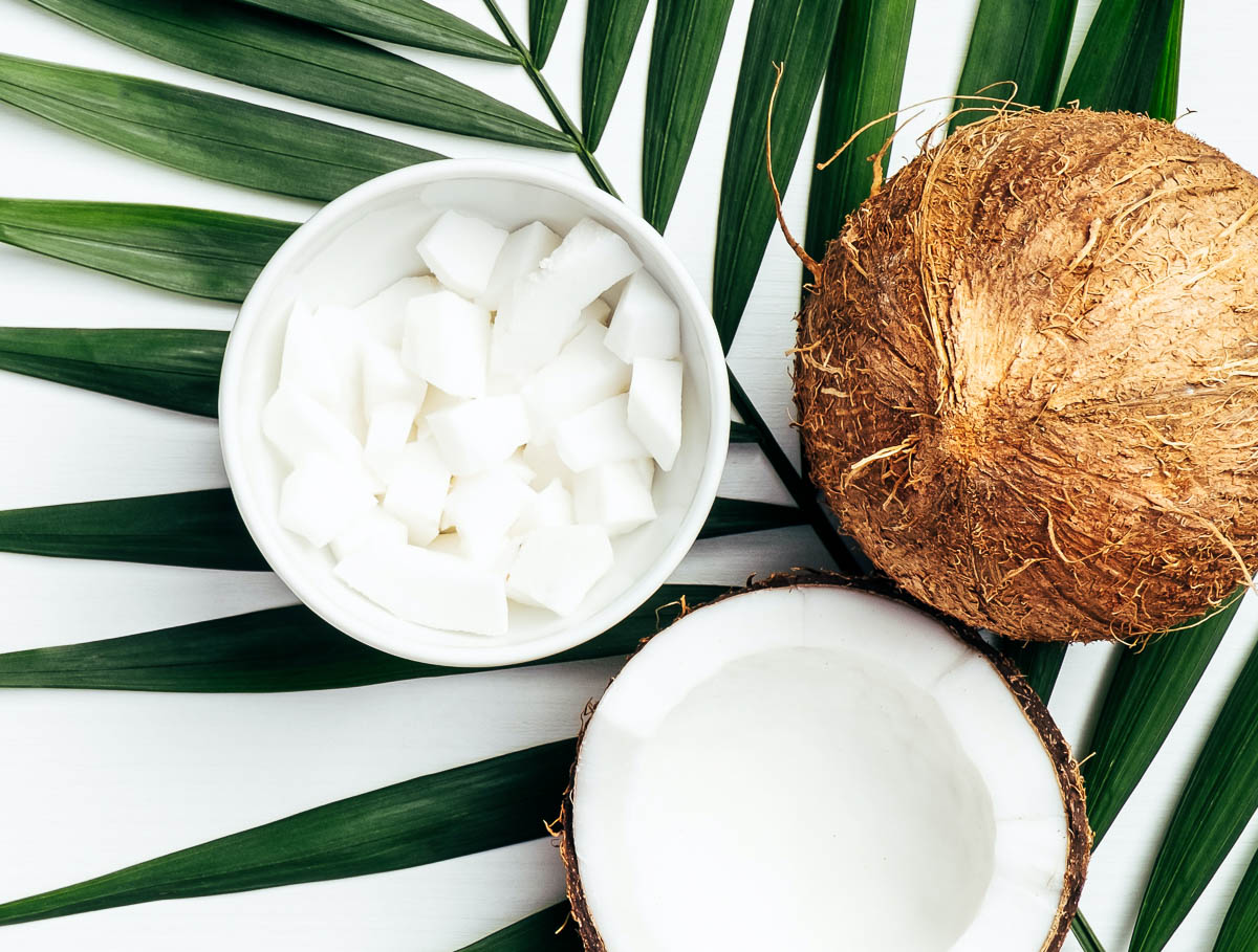 white bowl of cubes of coconut flesh next to 2 halves of fresh coconut.