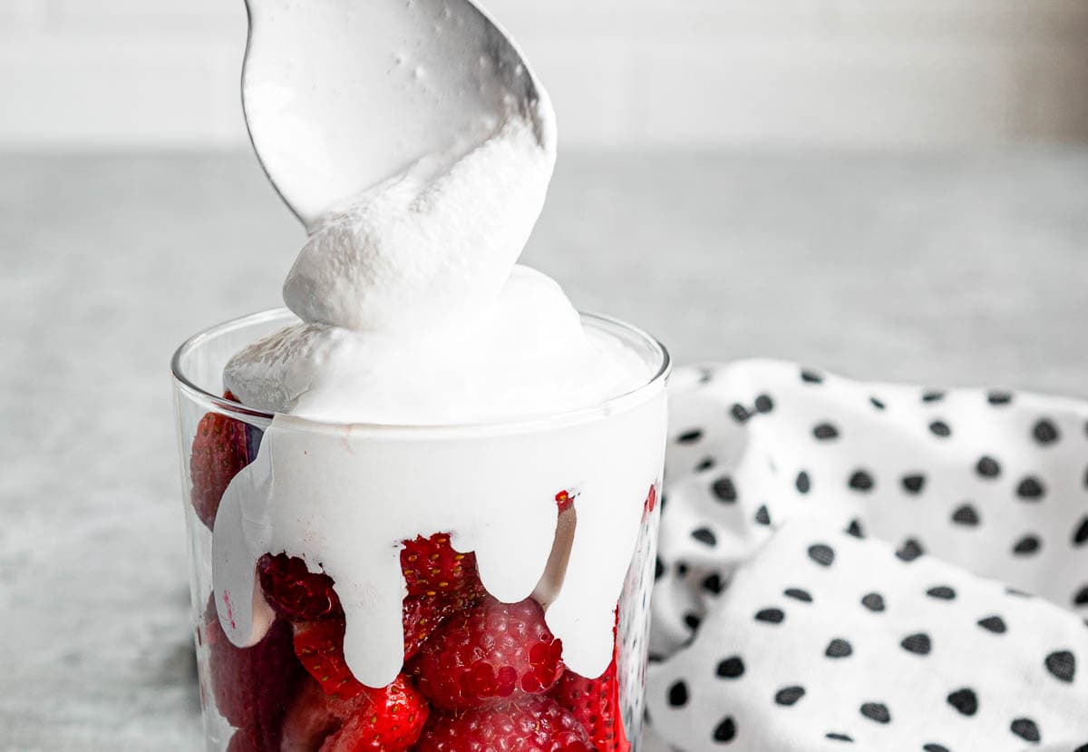 fresh vegan whipped topping over fresh berries in glass.