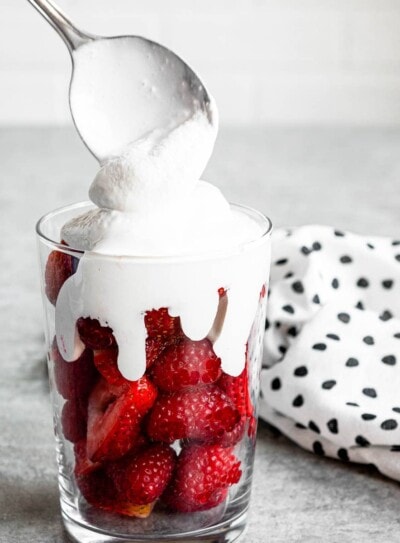 dairy-free coconut whipped cream getting scooped over fresh strawberries in a clear glass.