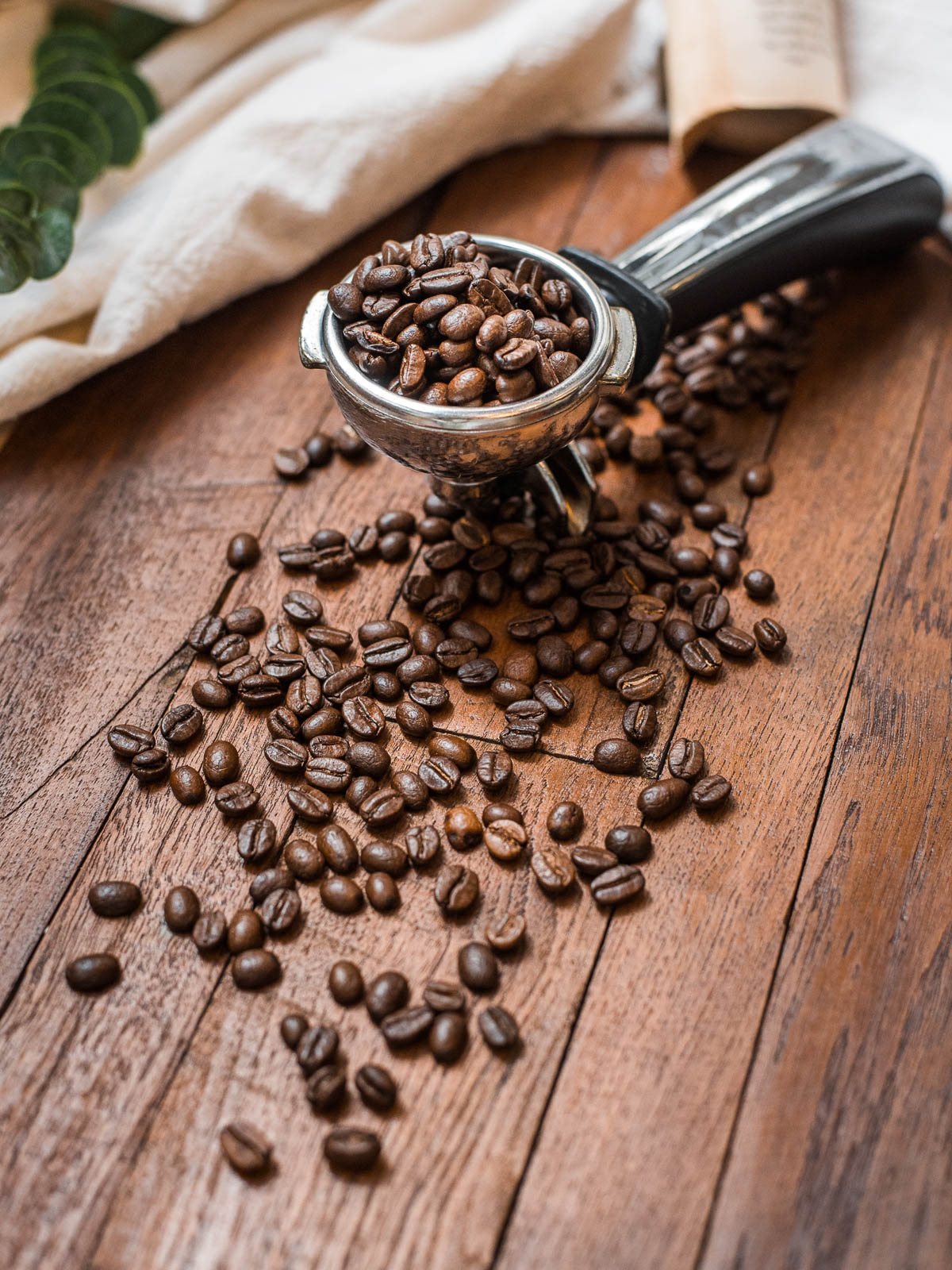 whole coffee beans spilling out of a coffee scoop on a wooden table.