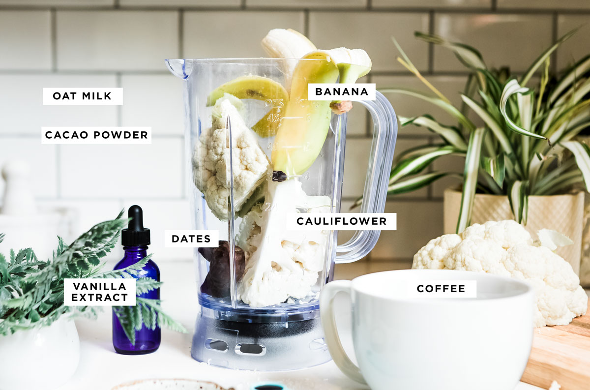 labeled ingredients for a coffee smoothie including banana, oat milk, cacao powder, dates, cauliflower, vanilla extract and coffee.