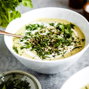 White bowl of celery soup on a table with bunch of fresh parsley.