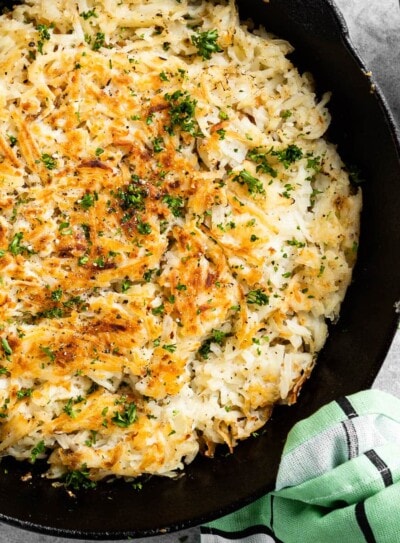 black skillet of crispy hash browns topped with fresh parsley.