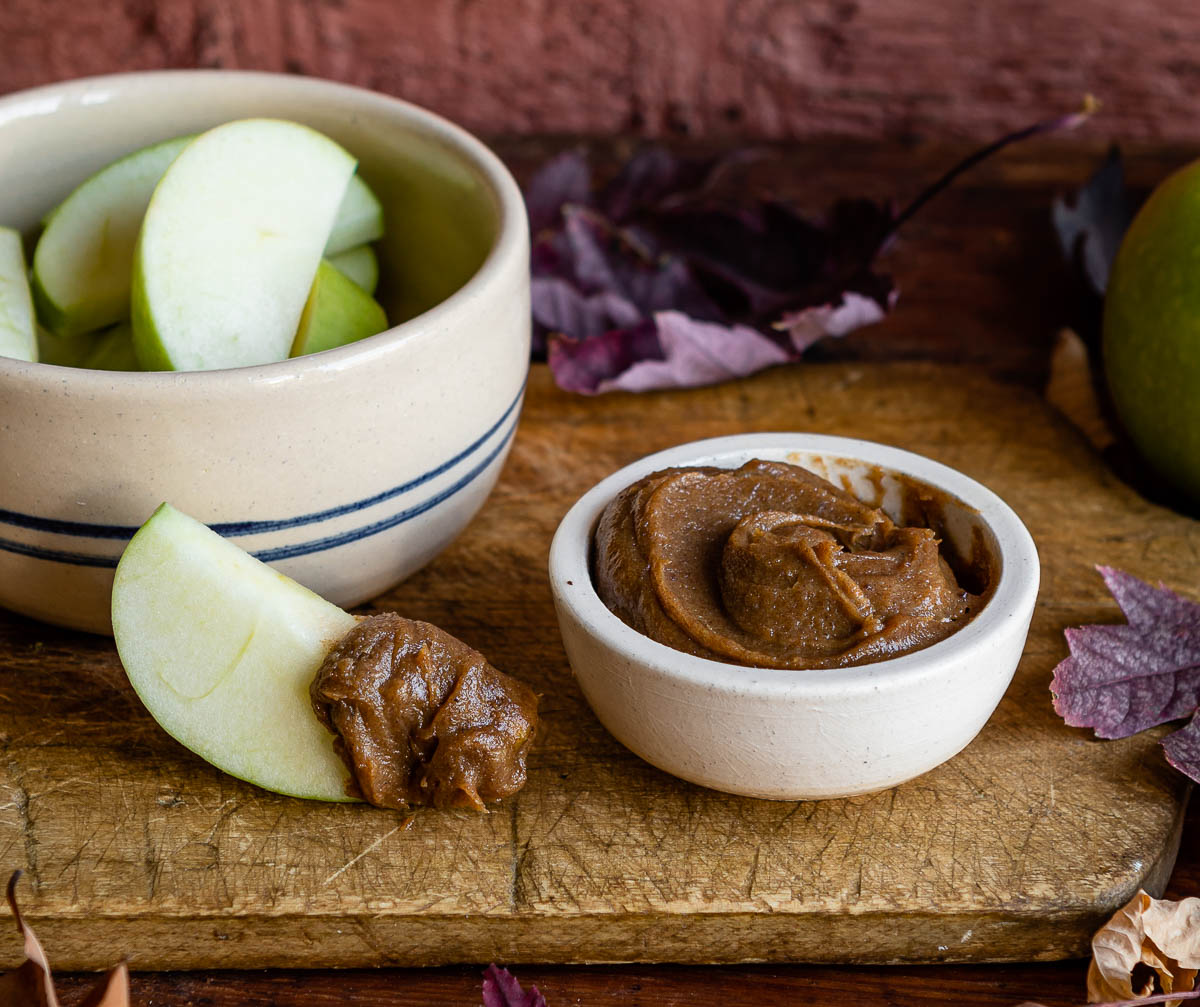 white bowl of healthy apple dip next to a bowl of apple slices and one apple with dip on it.