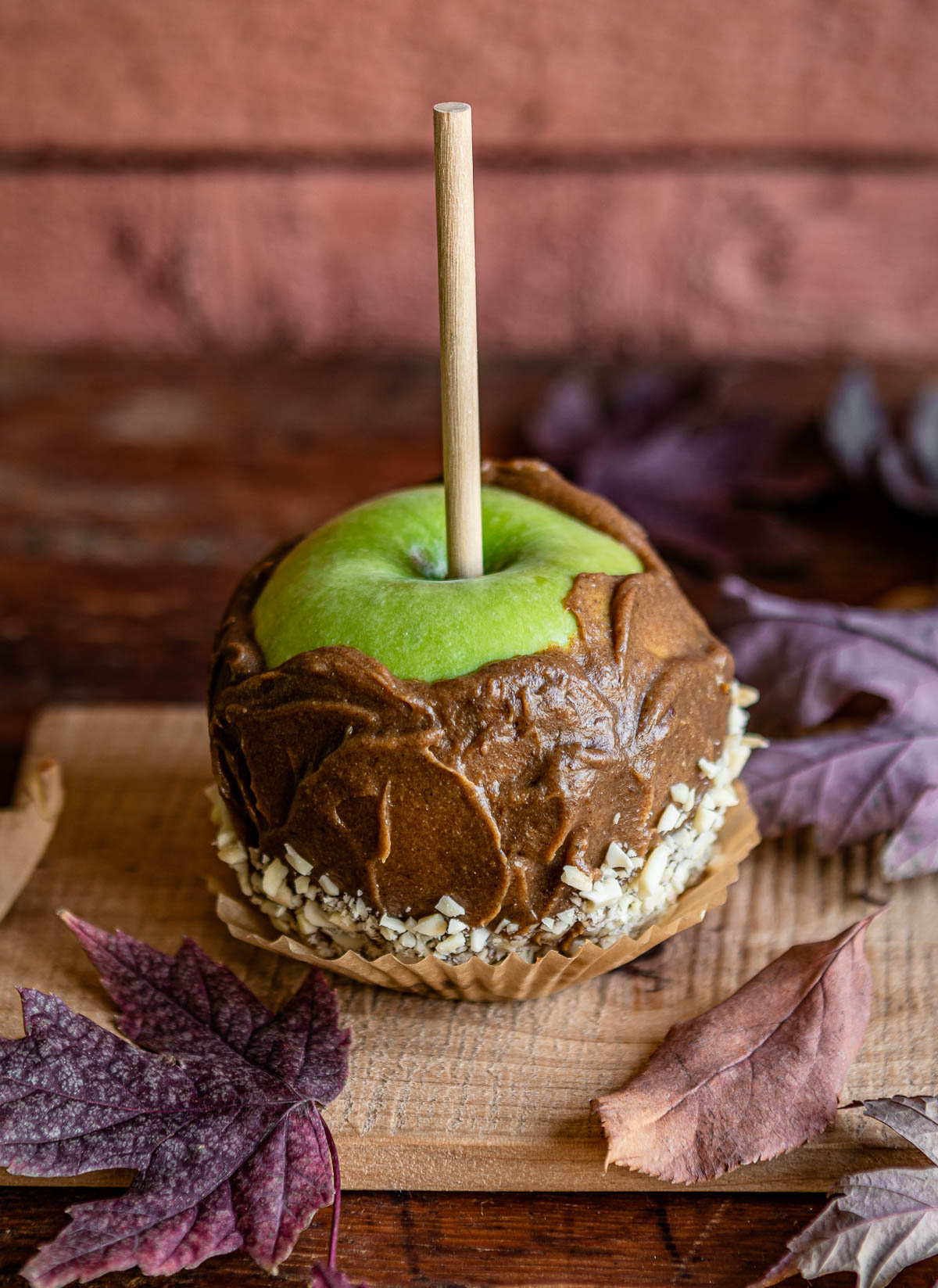 date caramel covered green apple with wooden stick in it and crushed nuts sitting on a paper.