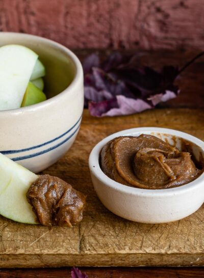 white bowl of date caramel next to striped bowl of sliced green apples on wooden counter.