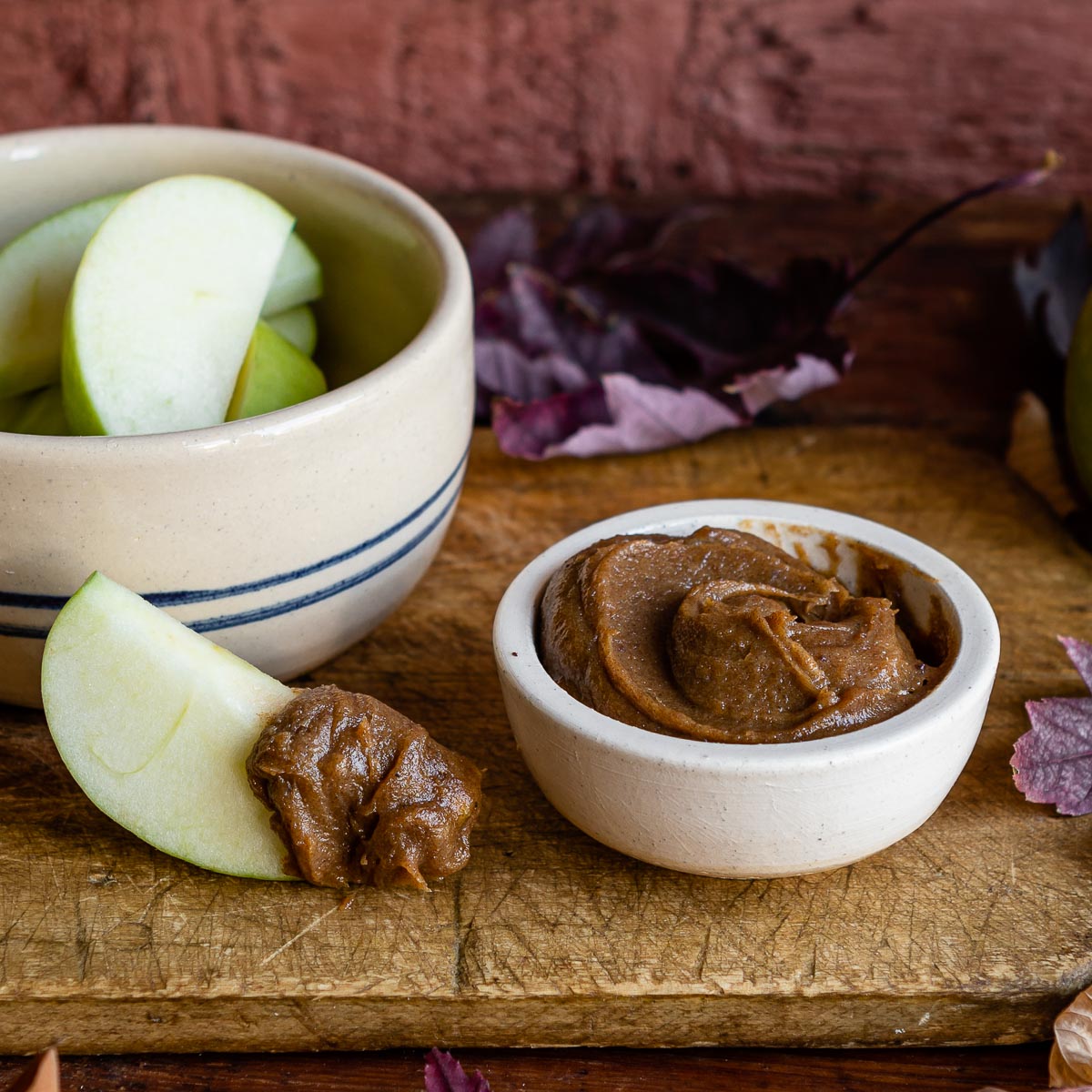 white bowl of date caramel next to striped bowl of sliced green apples on wooden counter.