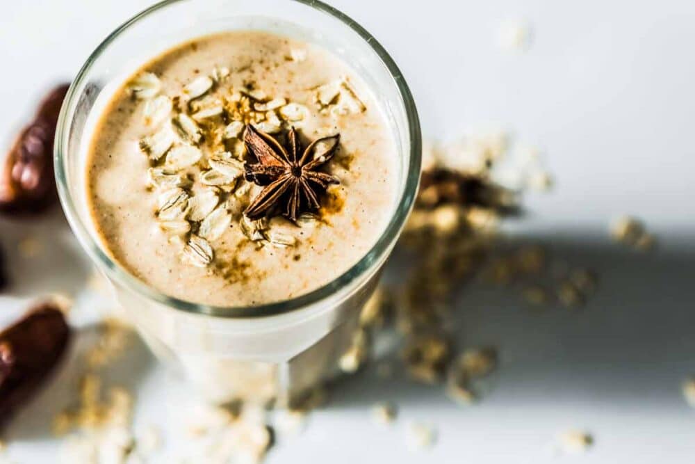 Healthy date smoothie topped with rolled oats and star anise, with oats and dates scattered on the countertop.