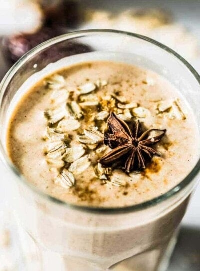 Cinnamon Date Smoothie, topped with oats and star anise, in a tall, clear glass.